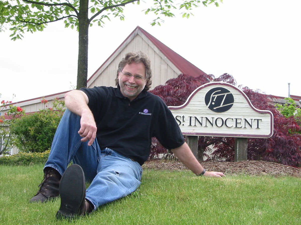 Mark Vlossak sitting in the grass in front of the St. Innocent sign